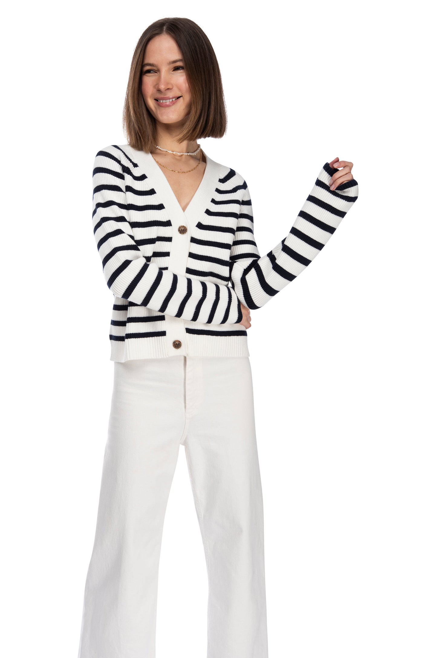A confident young woman in a LS Stripe Cardigan from B Collection by Bobeau and white pants posing with one hand on her hip against a white background.