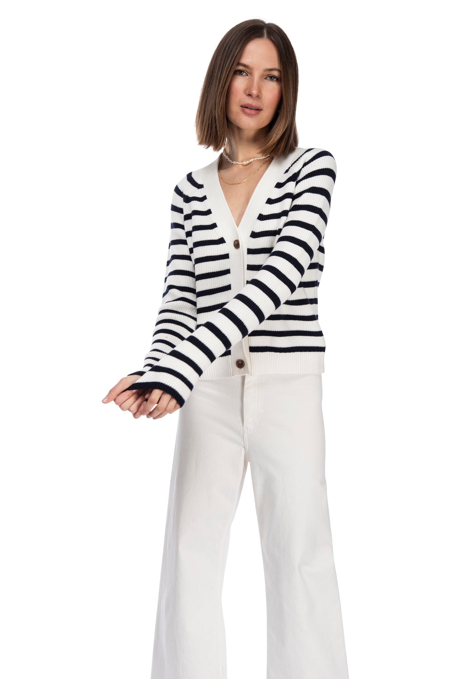 A woman stands on a white background, dressed in a chic black and white LS Stripe Cardigan crafted from super soft yarn by B Collection by Bobeau, paired with white pants, presenting a relaxed yet fashionable look.