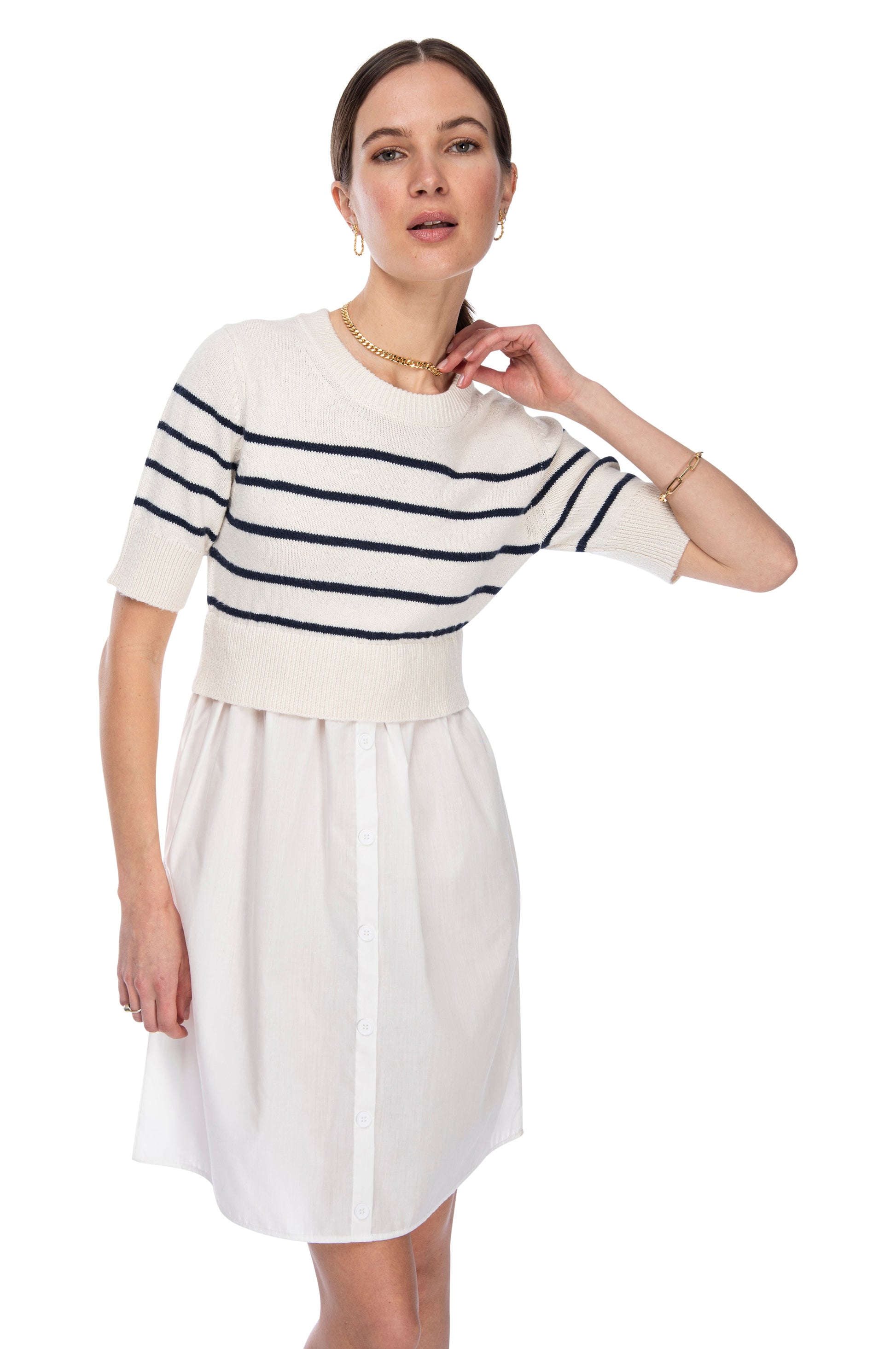 A woman posing with her hand on her neck, wearing a stylish cream poplin skirt and a short-sleeved B Collection by Bobeau mixed media dress, accessorized with a gold necklace and bracelet.