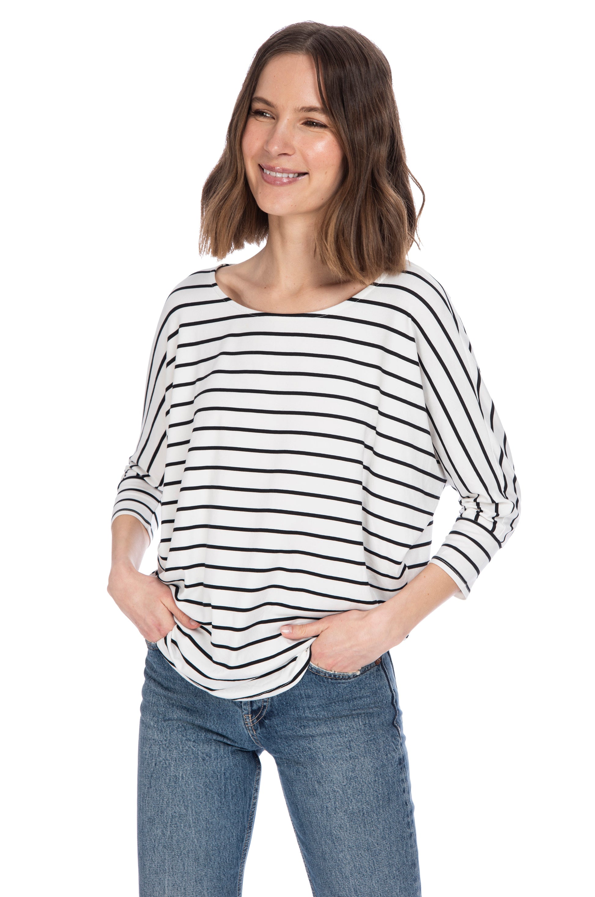 A smiling woman in a casual striped B Collection by Bobeau 3/4 SLV DOLMAN BUTTER TOP and blue jeans standing confidently with one hand in her pocket.
