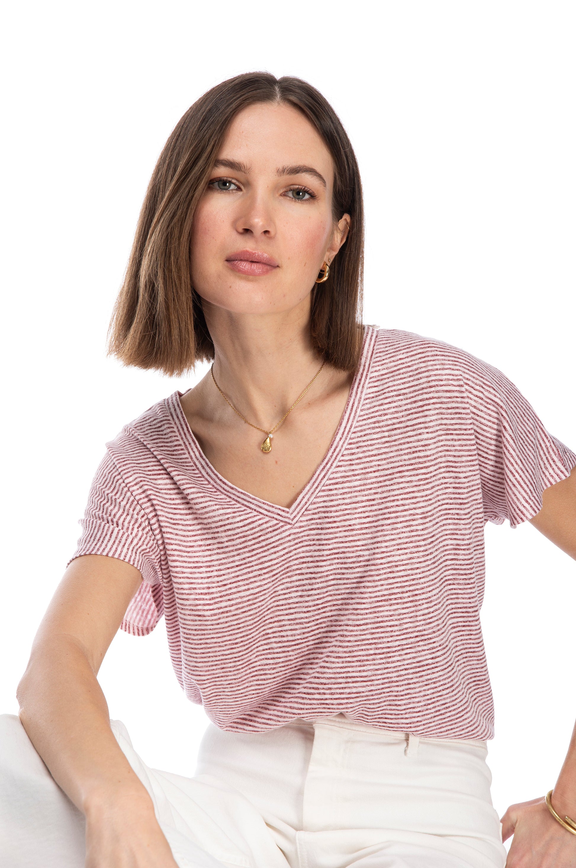 A woman with a confident gaze, wearing a casual striped CATY RELAXED tee by B Collection by Bobeau and white pants, poses for the camera against a white background.
