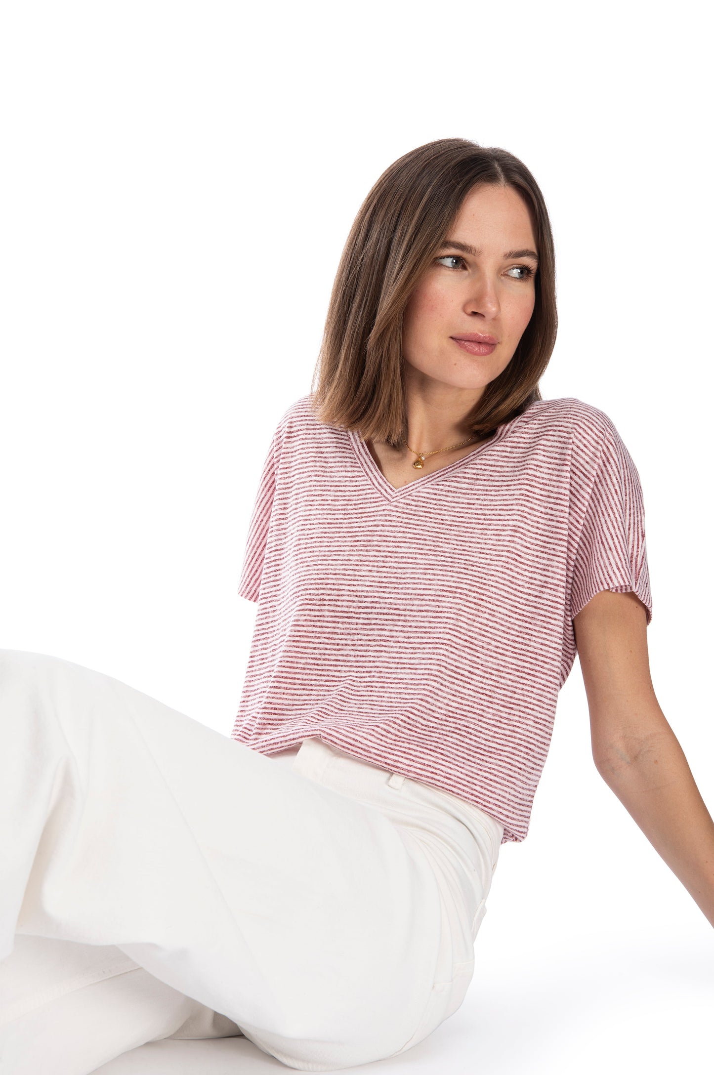 Woman in a B Collection by Bobeau Caty Relaxed Tee, V-neck tee, and white pants posing with a contemplative gaze against a white background.