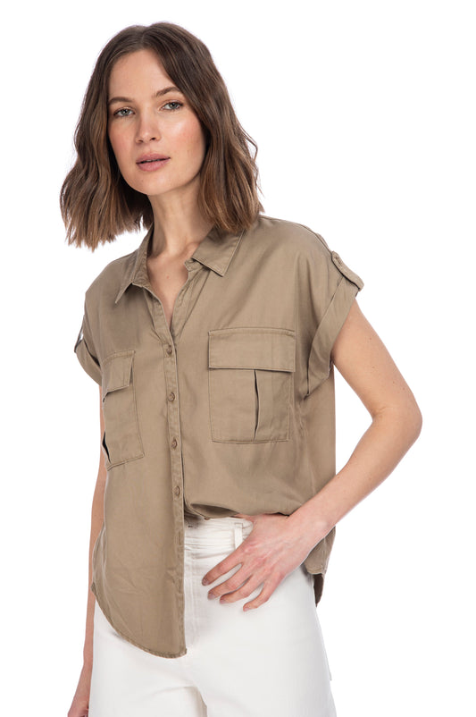 A woman wearing a casual khaki B Collection by Bobeau Utility Button Up top with rolled-up sleeves and white pants, posing against a white background.