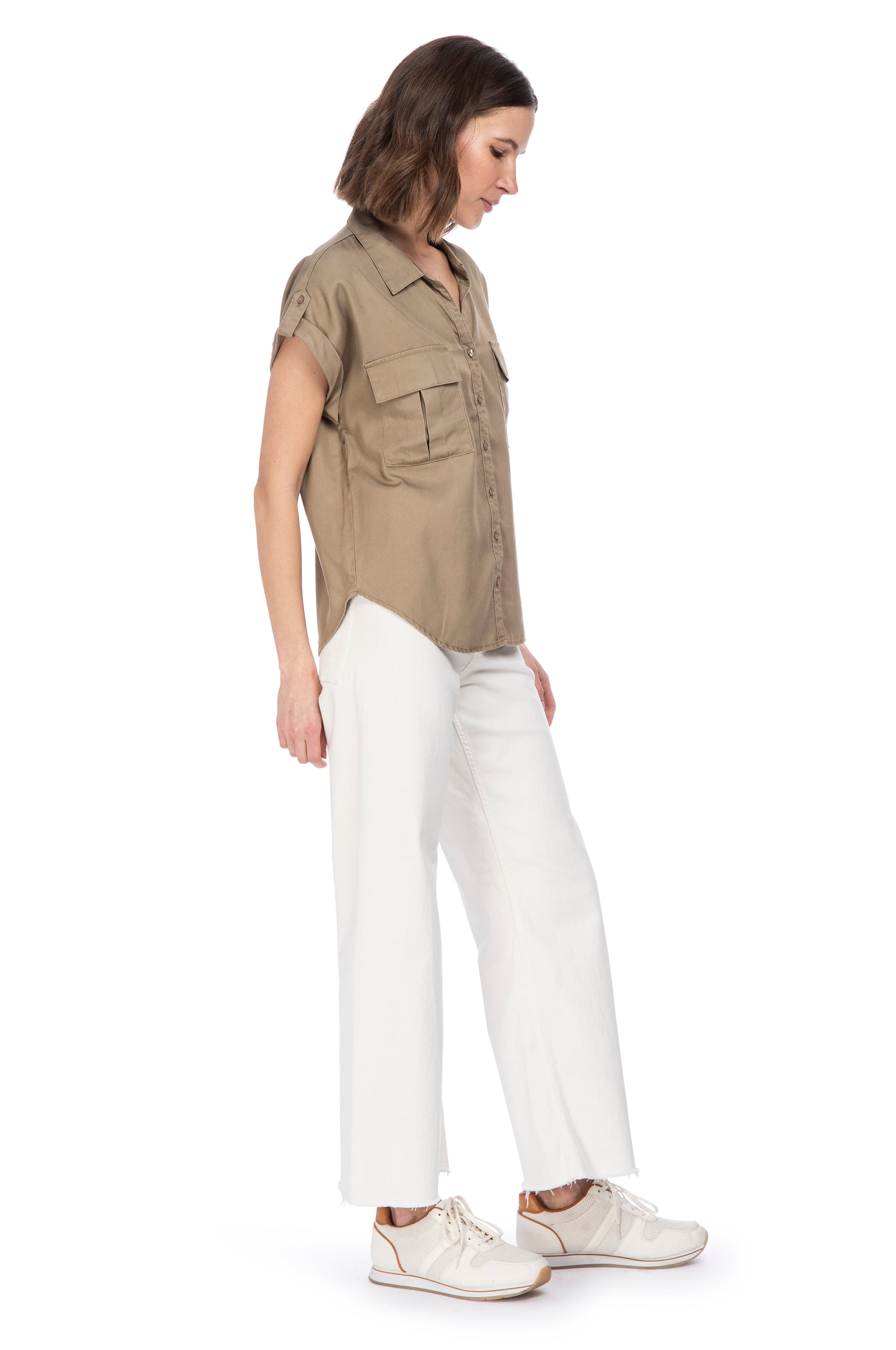A woman in a casual chic outfit with a B Collection by Bobeau Utility Button Up top in khaki and white trousers, paired with white sneakers.