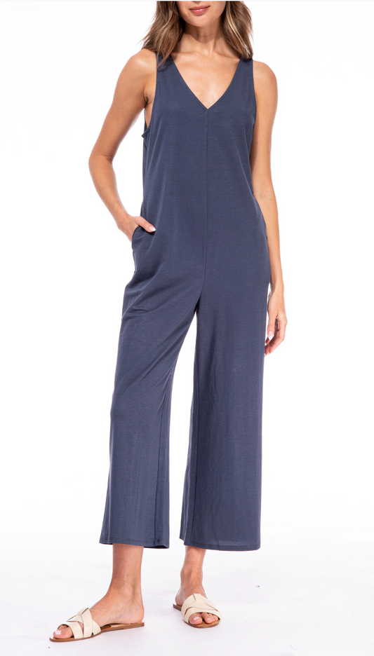 Woman posing in a chic B Collection by Bobeau sleeveless V neck jumpsuit in navy blue with wide-leg pants, paired with white sandals.