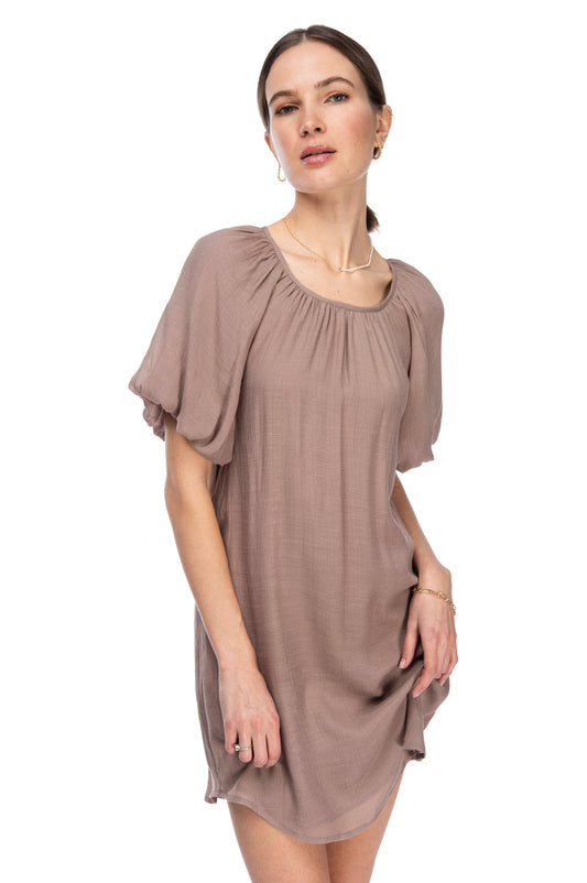 Woman posing in a simple, elegant taupe gauze B Collection by Bobeau dress with bubble hem sleeves and a round neckline, against a white background.