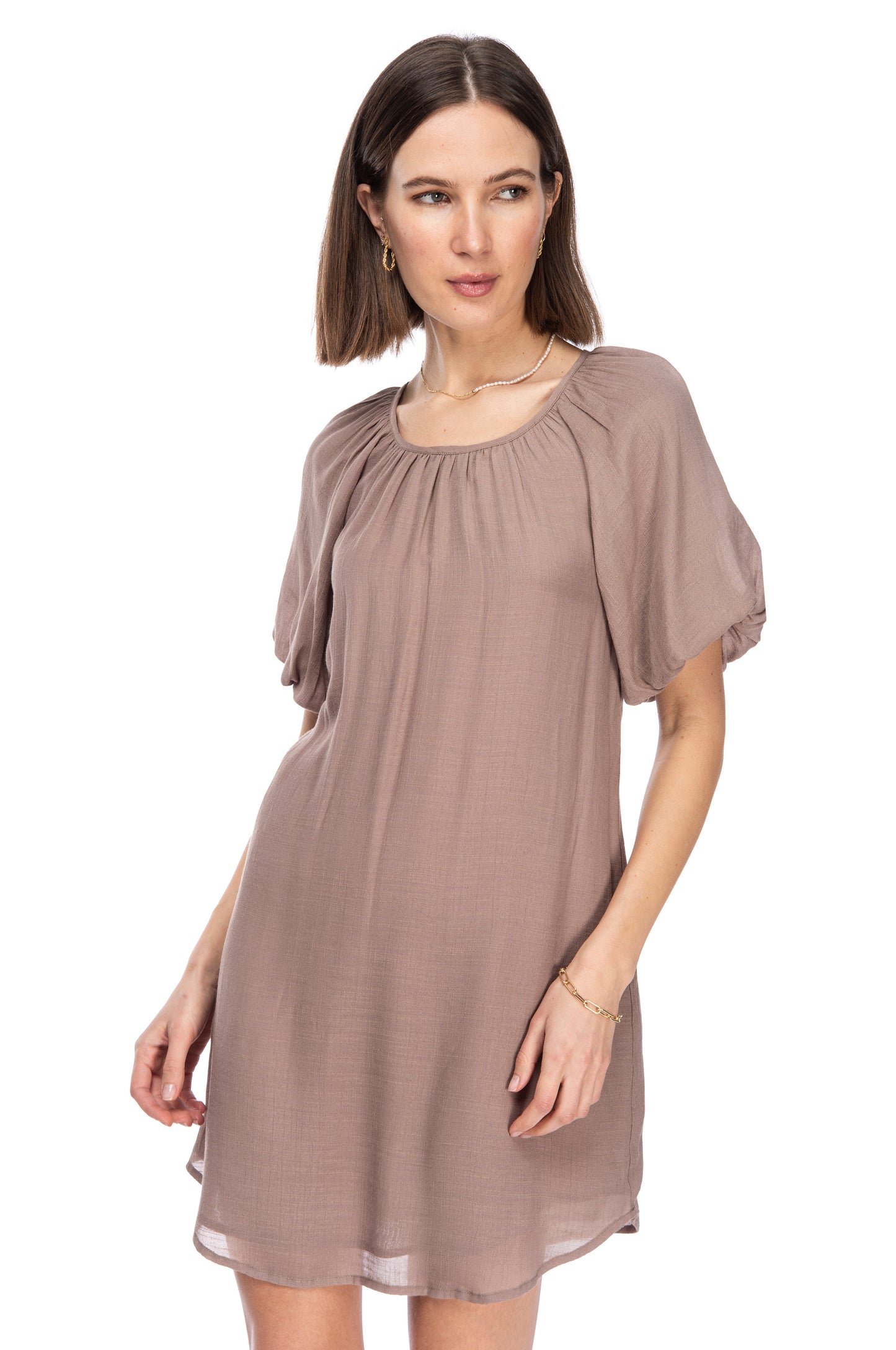 A woman modeling a taupe gauze B Collection by Bobeau dress with bubble sleeves and a round neckline, posing for a fashion shoot.