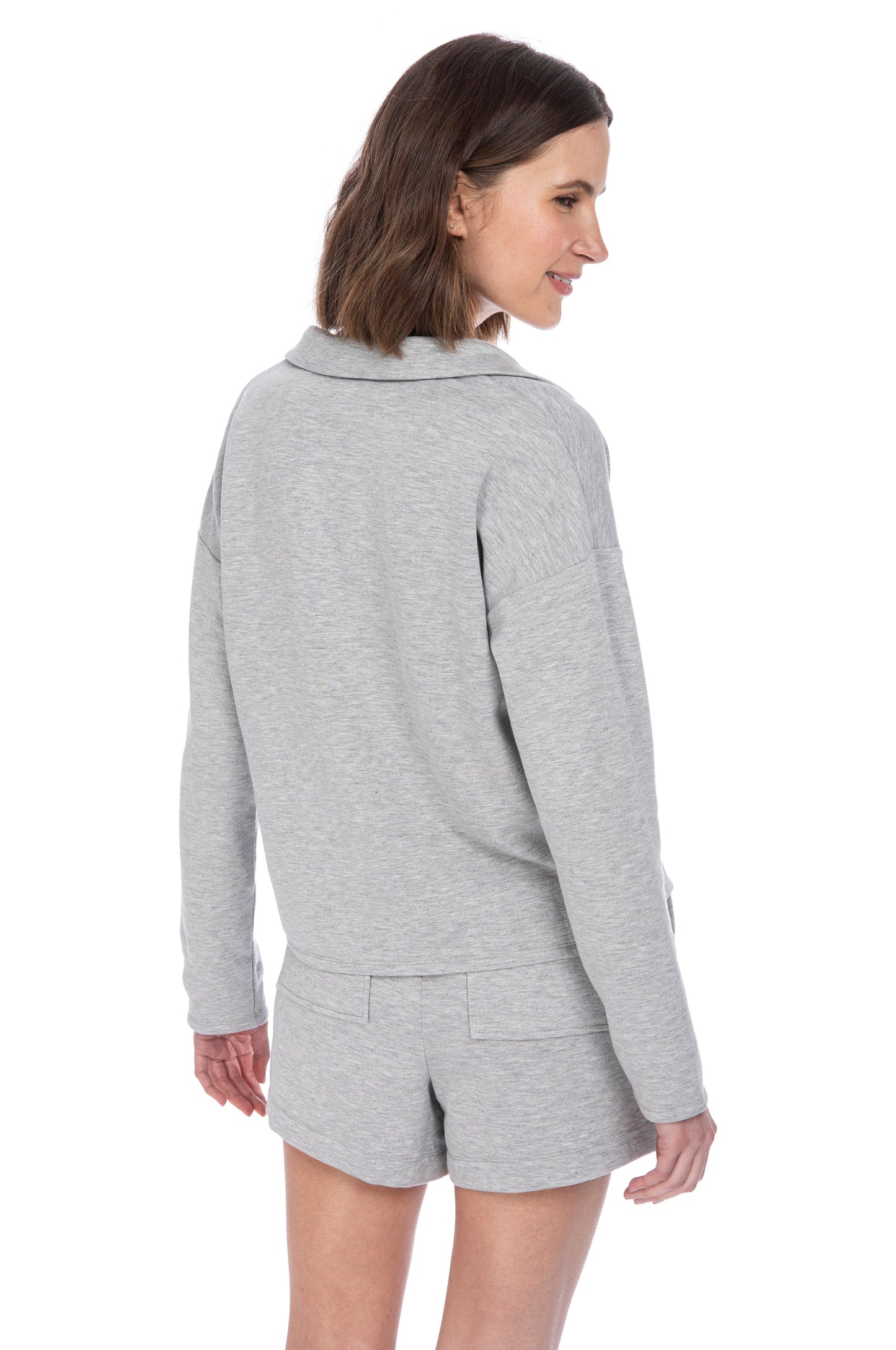 Woman in a casual B Collection by Bobeau Stella Fleece grey hoodie and shorts smiling and looking to the side, showcasing the back of the outfit.