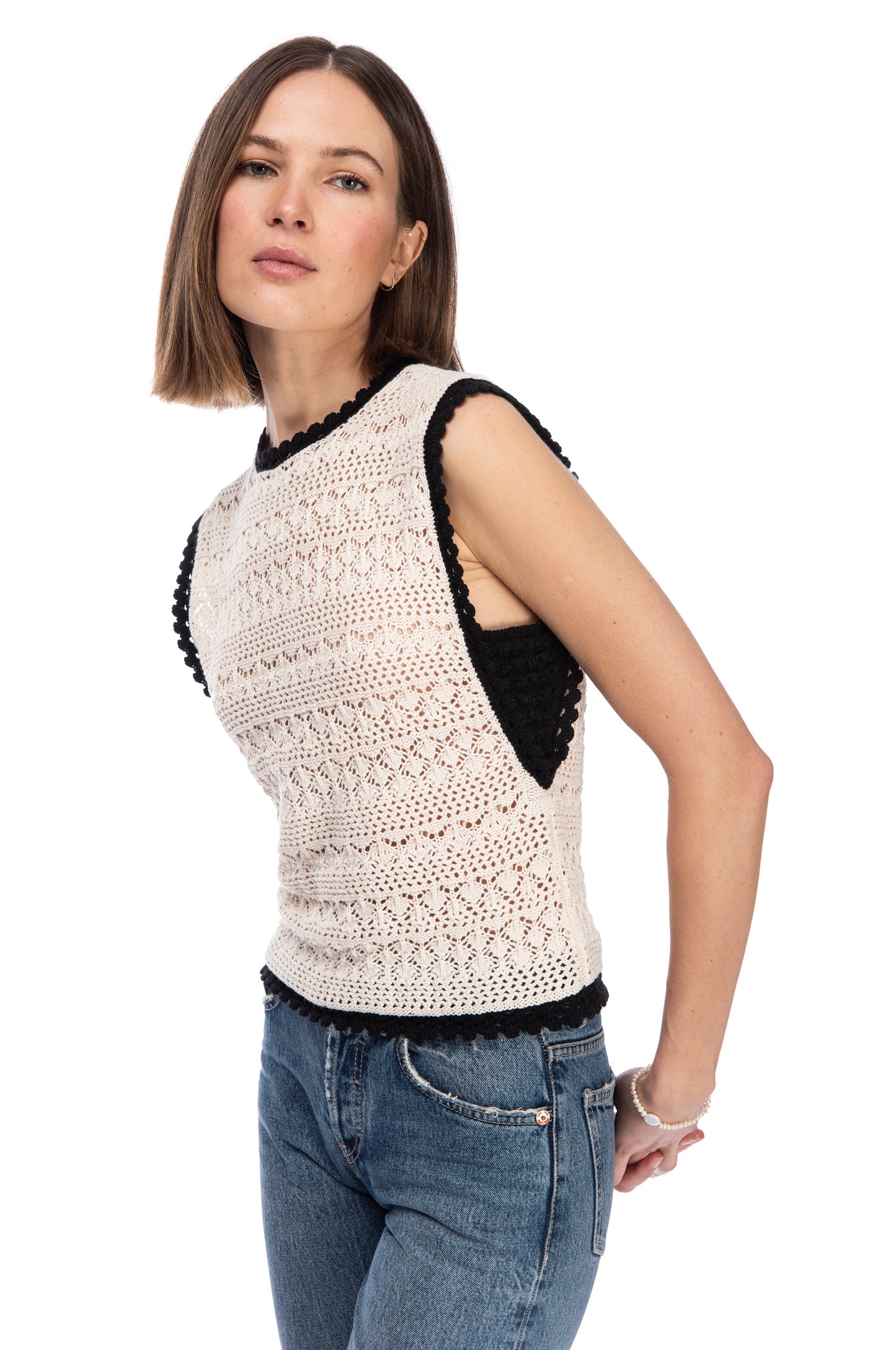 Woman posing in a stylish B Collection by Bobeau SLVLSS CROCHET SWEATER TOP with scalloped edges and classic blue jeans against a white background.