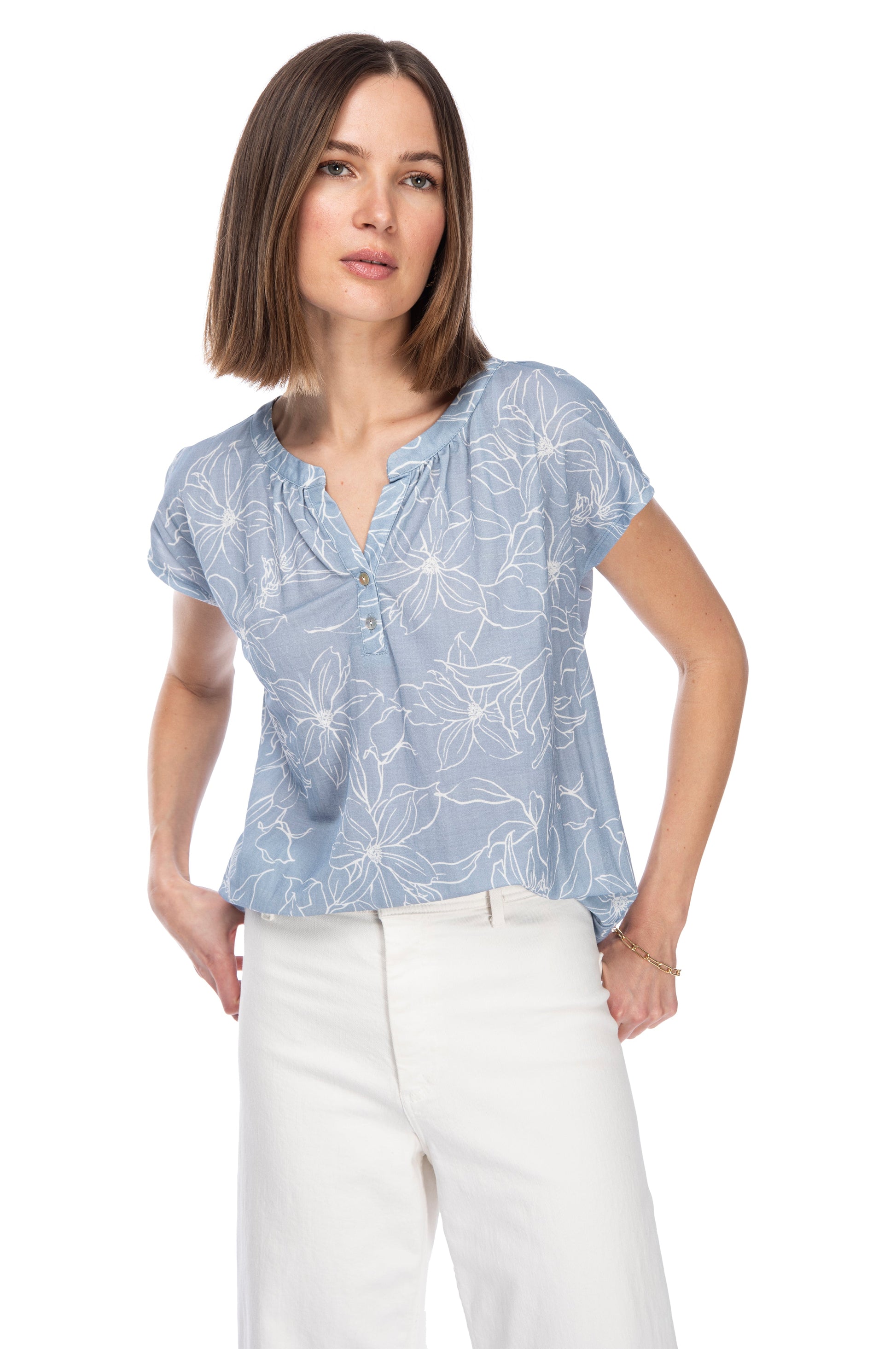 A woman in a casual blue floral SHIRTTAIL BTTN PULLOVER TOP with a notch neckline and white pants posing against a white background. Brand Name: B Collection by Bobeau