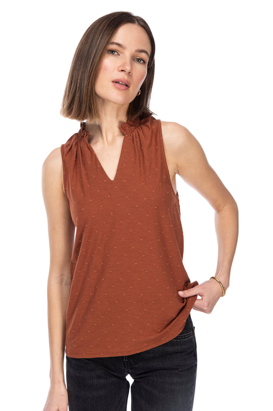 A woman in a sleeveless rust-colored RUFFLE NK TANK TOP by B Collection by Bobeau and jeans posing confidently against a white background.