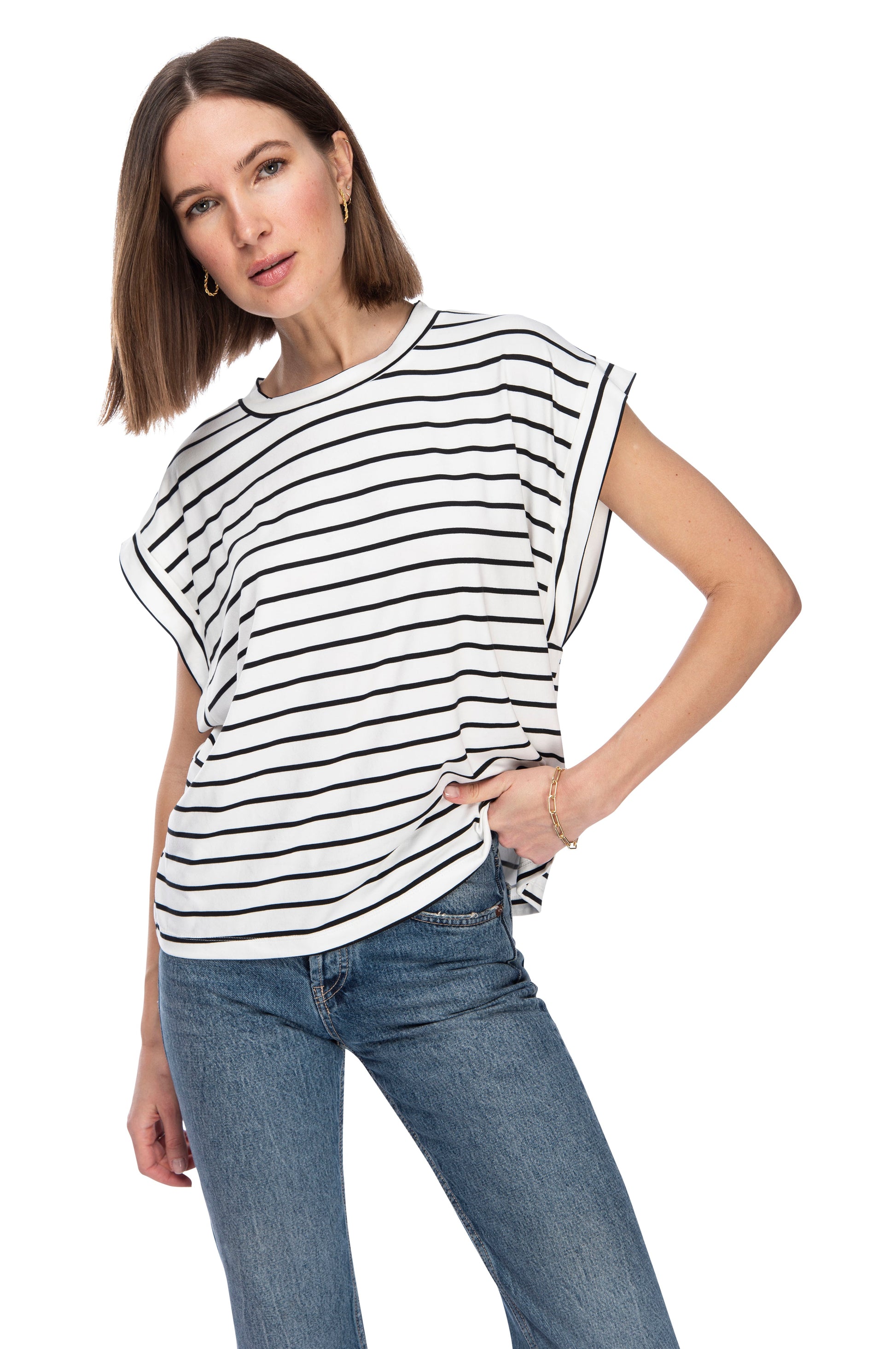 A woman in a casual DROP ARMHOLE TEE by B Collection by Bobeau and jeans posing confidently with one hand on her hip.