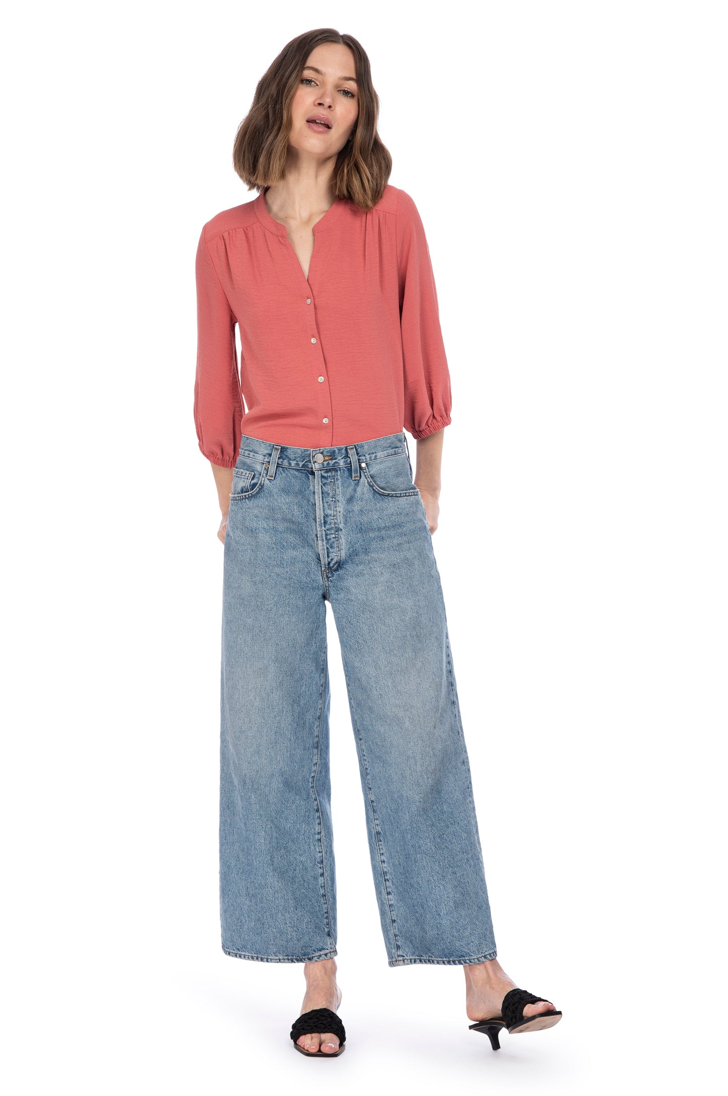 A woman standing confidently in a casual chic outfit, featuring a rust-colored, 100% Polyester RIVER BUTTON UP BLOUSE by B Collection by Bobeau paired with classic wide-leg denim jeans and black open-toe heels.