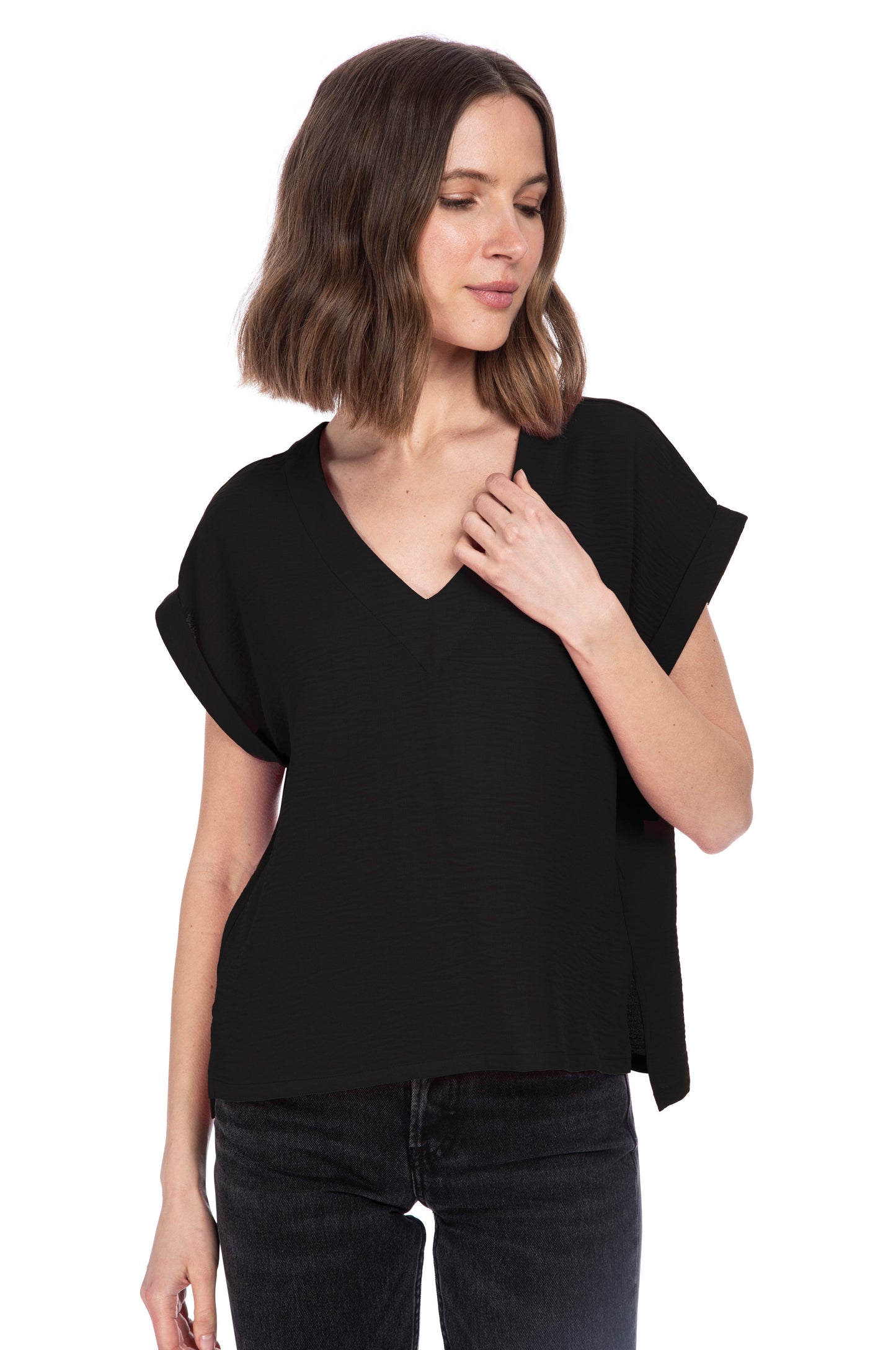 A woman with shoulder-length hair wearing a black V NECK RELAXED WOVEN TEE made of 100% Polyester and dark jeans against a white background by B Collection by Bobeau.