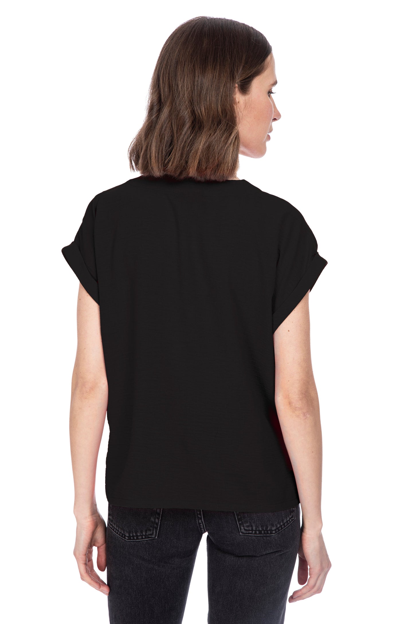 Woman standing with her back to the camera, wearing a V NECK RELAXED WOVEN TEE and dark jeans, fabricated from 100% Polyester for easy Machine Wash Cold by B Collection by Bobeau.