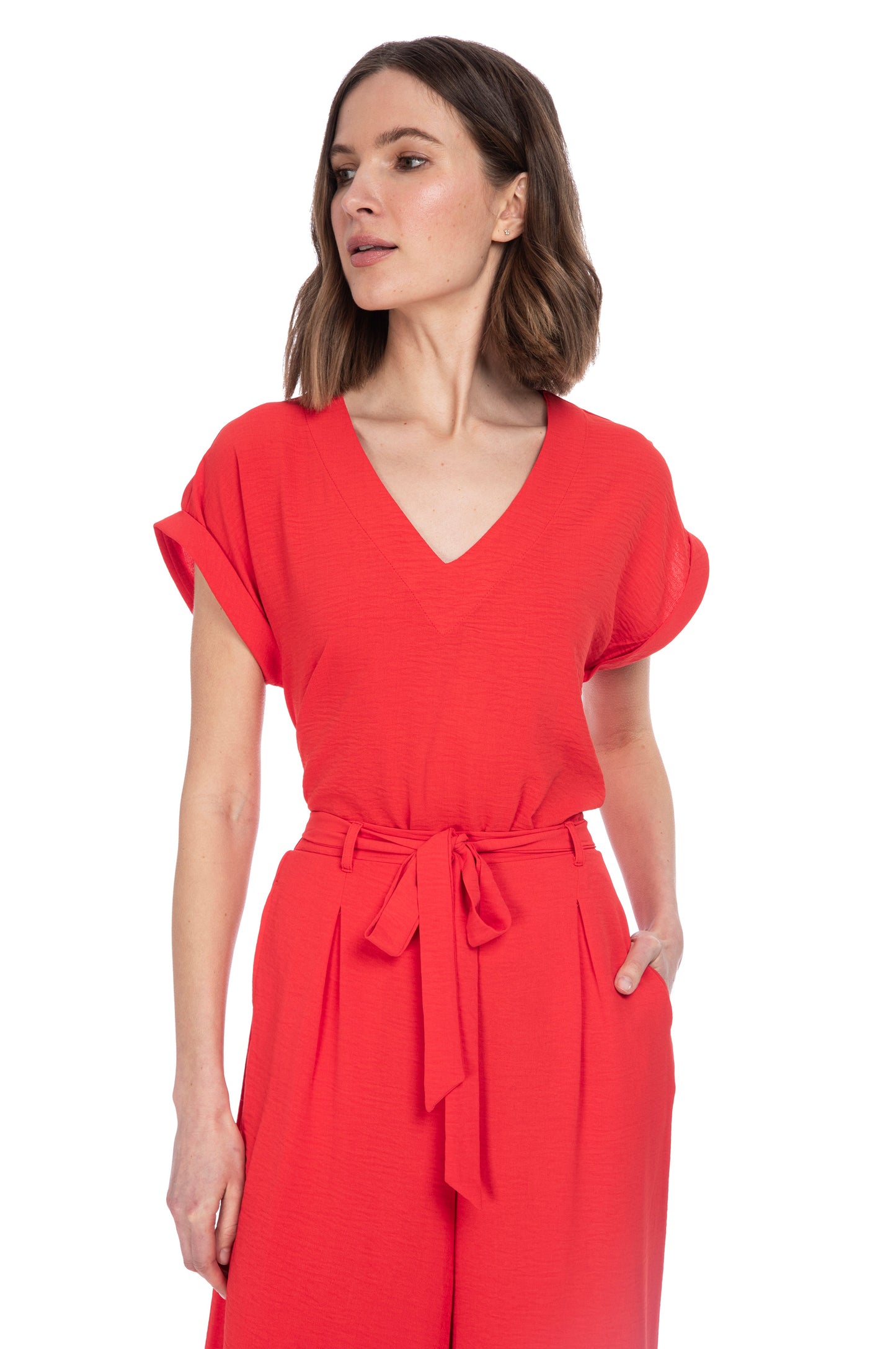 A woman in a stylish red jumpsuit with a v-neckline and waist-cinching tie belt, crafted from 100% Polyester, posing against a white background from B Collection by Bobeau.