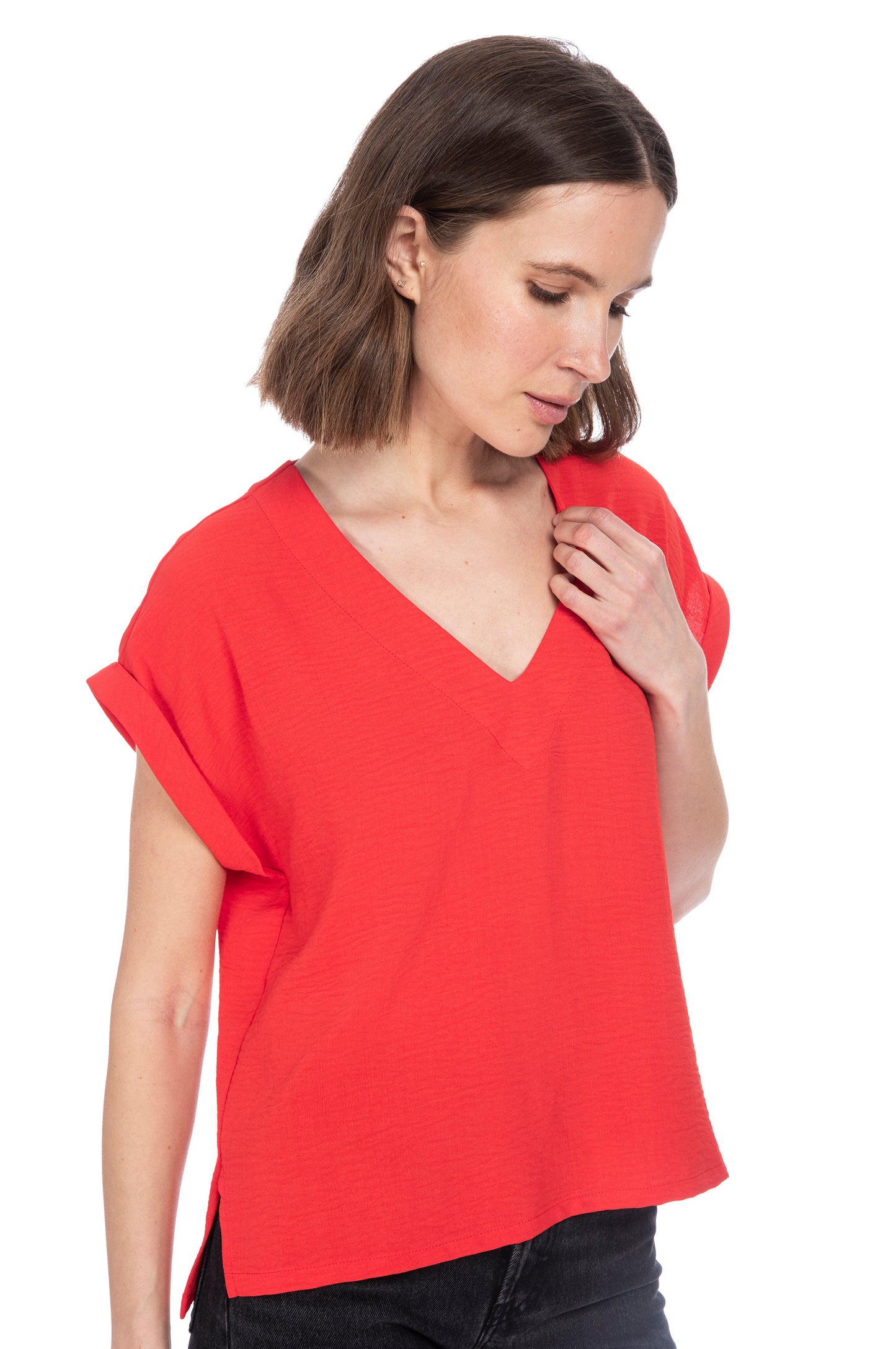 A woman with shoulder-length hair wearing a bright red V Neck Relaxed Woven Tee made of 100% Polyester, looking thoughtfully to the side against a white background by B Collection by Bobeau.