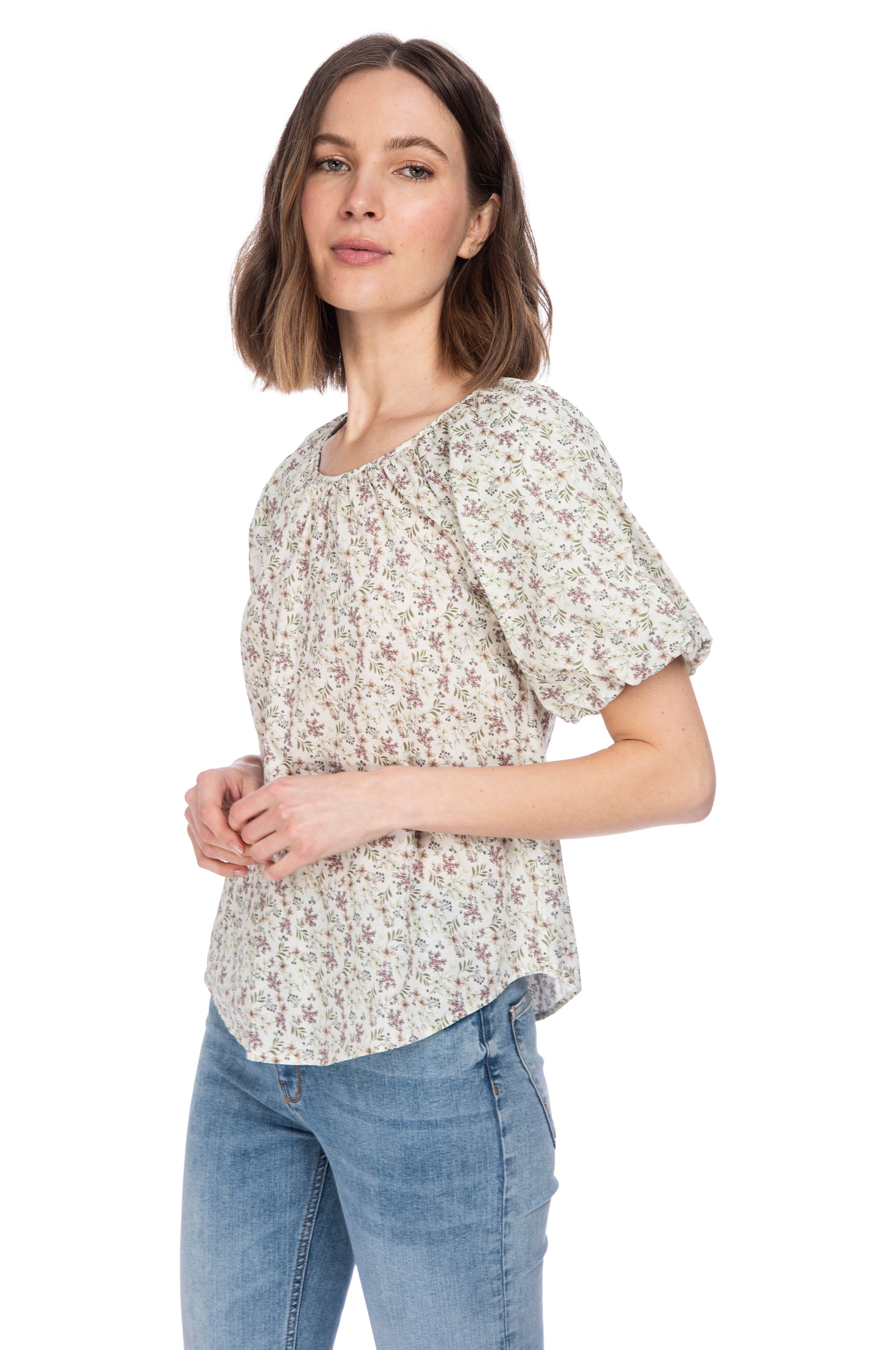 A woman confidently posing in a casual floral crewneck B Collection by Bobeau bubble sleeve cotton top and blue jeans, projecting a relaxed yet stylish vibe.