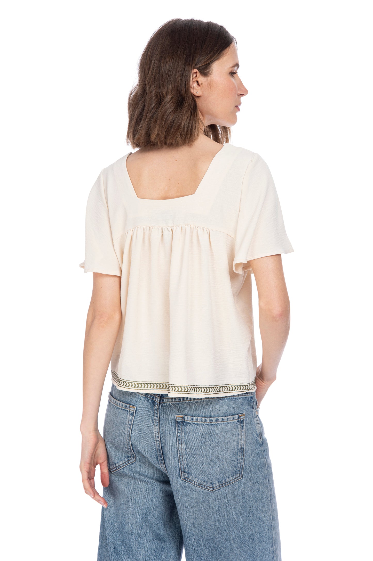 A woman seen from behind, wearing a casual beige short-sleeved SQUARE NECKLINE BOHO TOP with embroidery detail and blue denim jeans by B Collection by Bobeau.