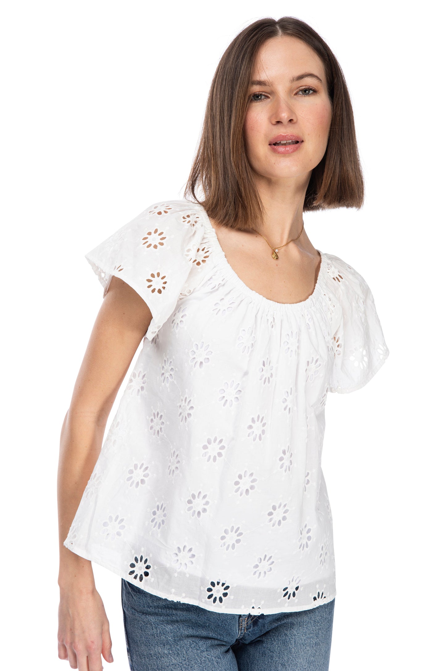 A woman wearing a B Collection by Bobeau SS PEASANT TOP, a 100% cotton, white blouse with floral cut-out patterns and an elastic neckline, looking directly at the camera with a neutral expression.