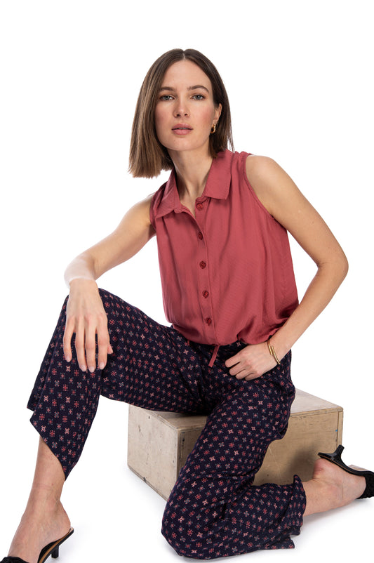 A confident woman posing in a sleeveless burgundy blouse and printed B Collection by Bobeau straight leg pants, with one hand resting on her hip and a relaxed yet assertive expression, isolated on a white background.