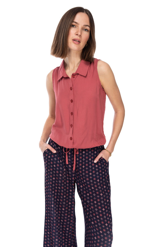 A woman in a B Collection by Bobeau SLVLSS BTTN DOWN TOP terracotta blouse and patterned pants standing with one hand on her hip against a white background.