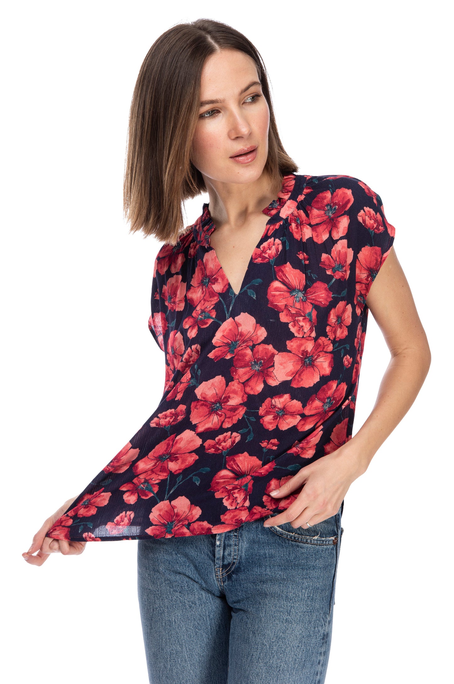 A woman in a floral printed, 100% Rayon Ruffle Neck Top and jeans, glancing to the side with a thoughtful expression from B Collection by Bobeau.