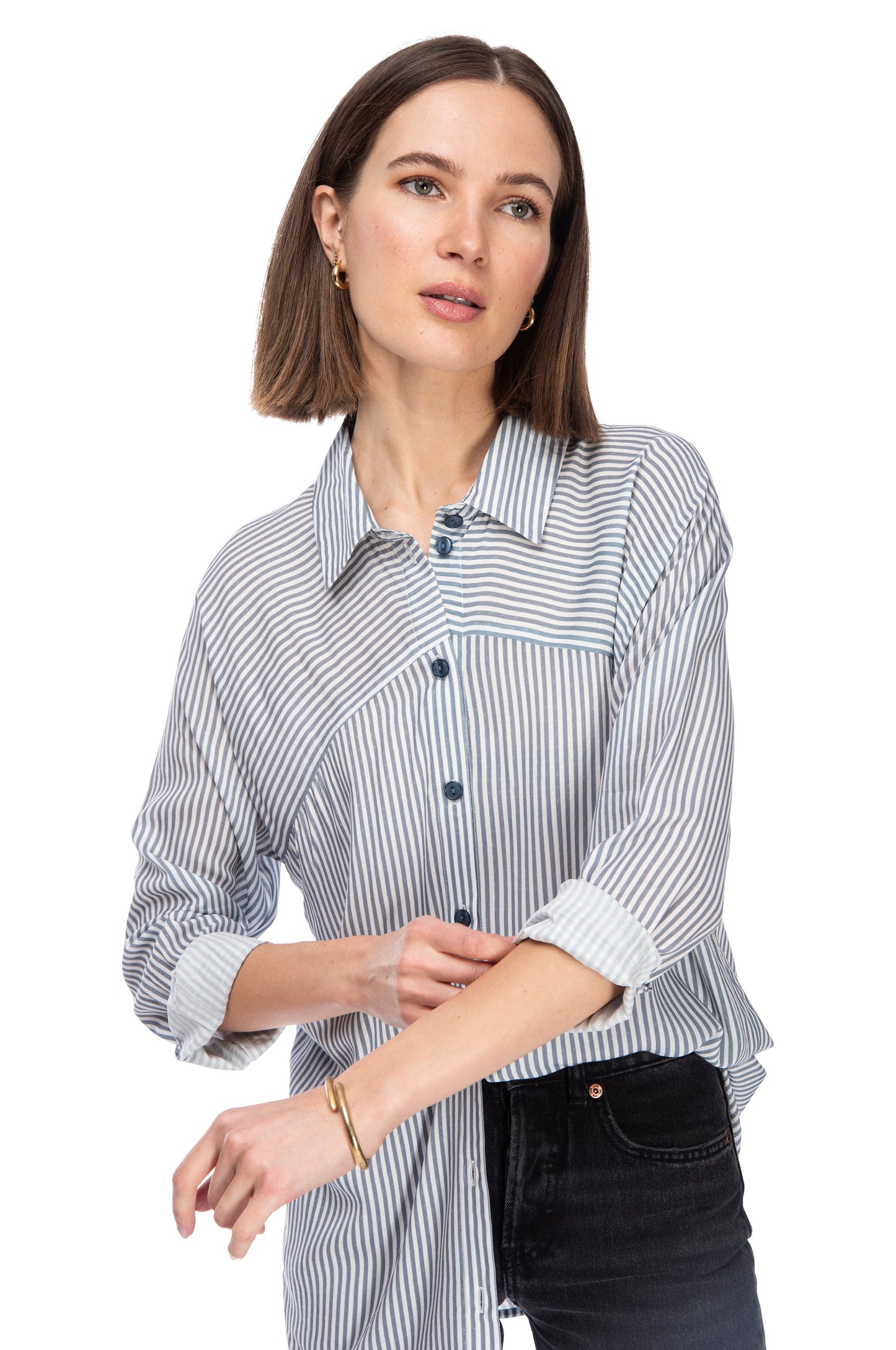 A woman with a subtle smile wearing a casual striped rayon LS BTTN DOWN TUNIC with rolled-up sleeves, accessorized with a simple bangle, posing against a white background. Brand Name: B Collection by Bobeau